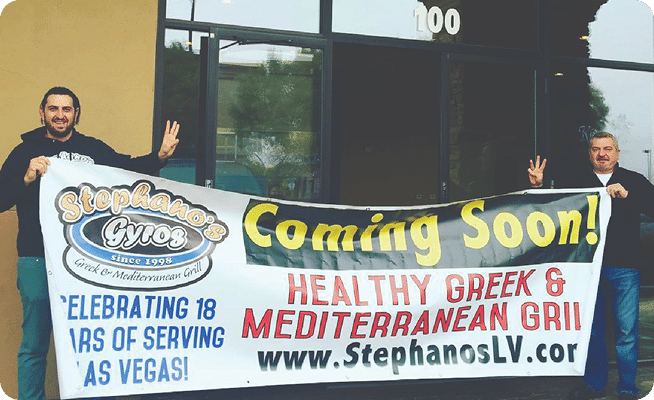 Two men hold a "Stephano's Gyros" banner that reads "Coming Soon! Healthy Greek & Mediterranean Grill."