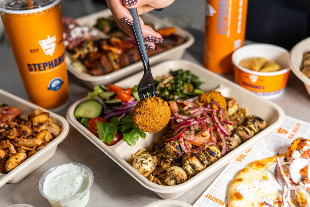 Stephano’s Greek And Mediterranean Grill opens fourth location 8 A hand with polka-dot nails holds a falafel ball over a meal of chicken, salad, and rice, with a "STEPHANIE'S" drink.